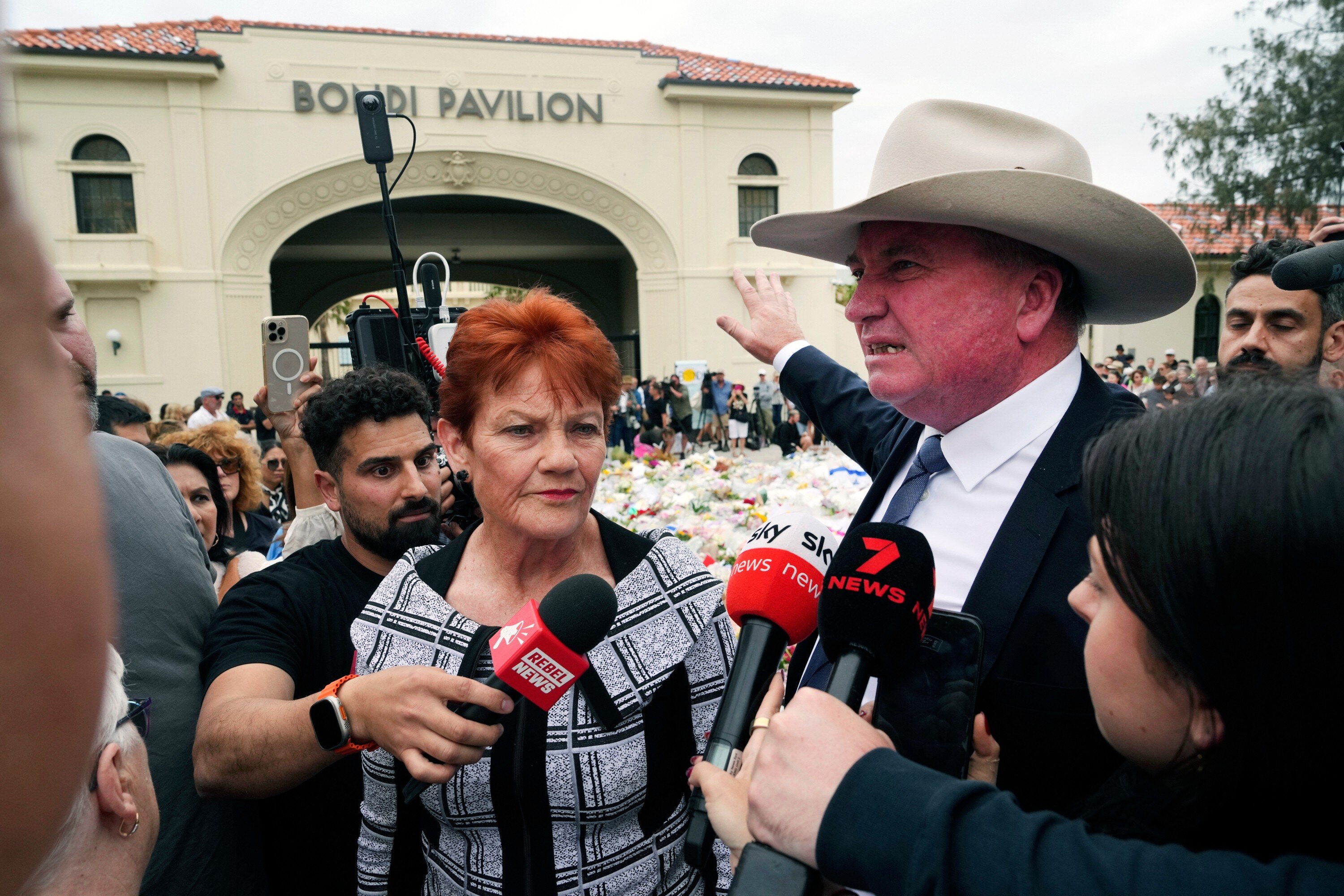 Australian politician's Pauline Hanson, center and Barney Joyce talk to the media at a floral tribute for shooting victims at the Bondi Pavilion at Bondi Beach on Tuesday, Dec. 16, 2025, following Sunday's shooting in Sydney, Australia. (AP Photo/Mark Baker)